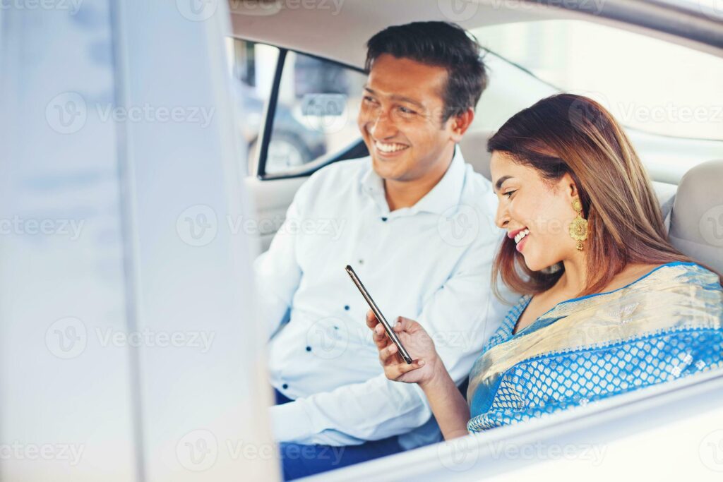 Indian man and woman using mobile phone app to book a taxi sitting on a passenger seat photo